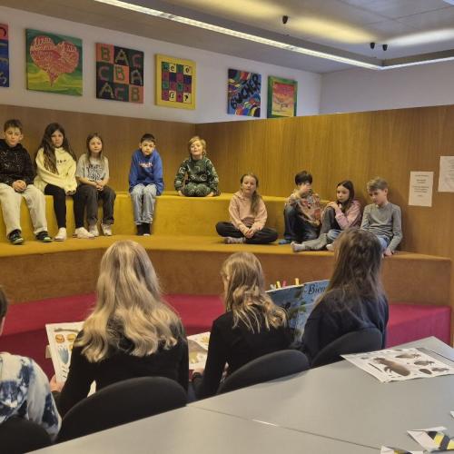 Mittelschülerinnen und Mittelschüler lesen Kindern aus einem Sachbuch vor