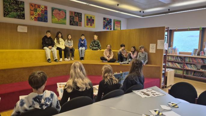 Mittelschülerinnen und Mittelschüler lesen Kindern aus einem Sachbuch vor